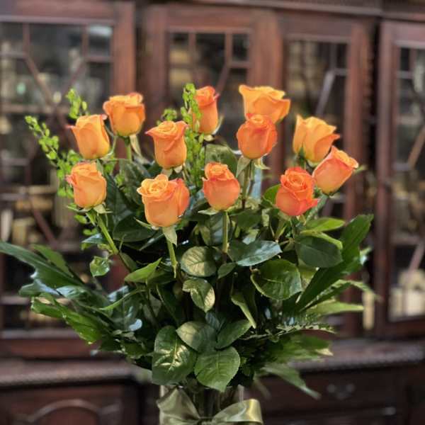 Tall arrangement of orange roses in a clear glass vase with a green ribbon bow