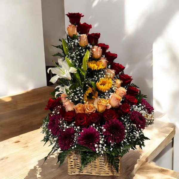 Tiered floral arrangement in a wicker basket with red and peach roses