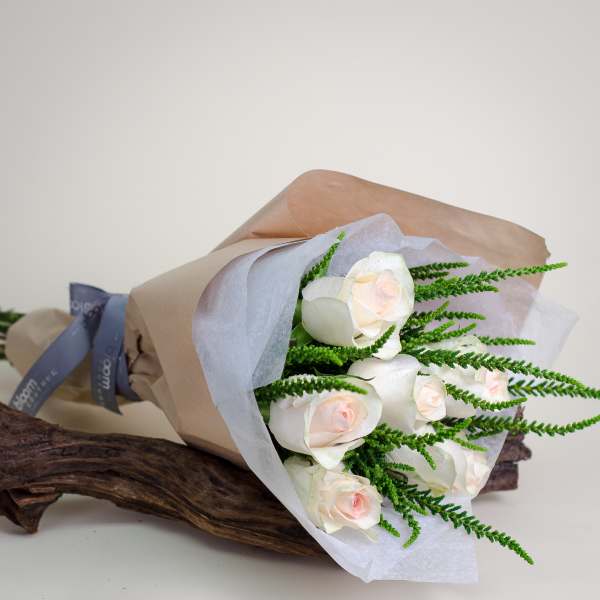 Bouquet of white roses wrapped in brown paper with green filler