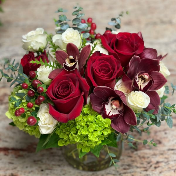 Red and white roses with burgundy orchids in a glass vase