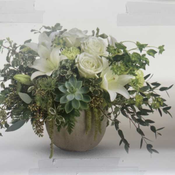 White lilies and roses in a round vase with trailing greenery