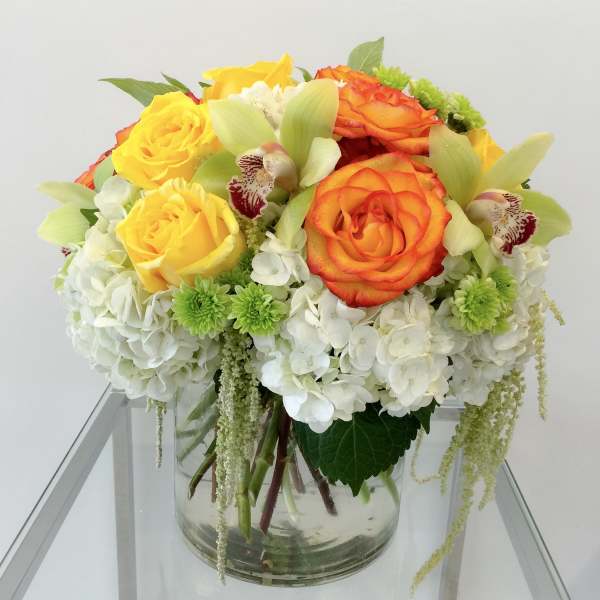 Bouquet of yellow and orange roses with white hydrangeas in a glass vase