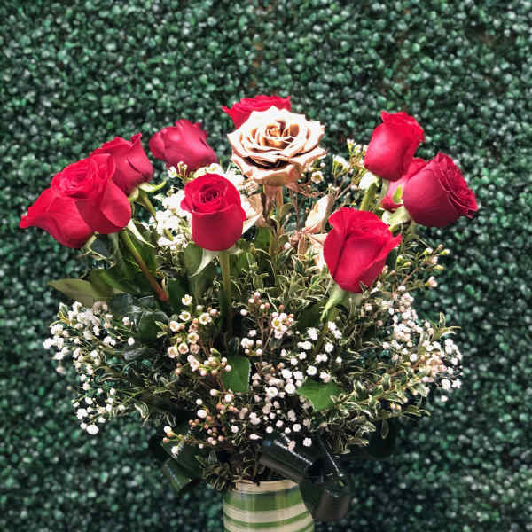 Tall vase of red roses with a single gold rose and white filler flowers in a striped green vase