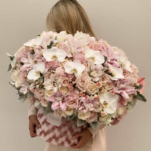 Large pastel bouquet of roses, orchids, and white blooms in a pink patterned box