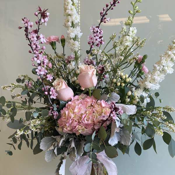 Tall pink and white floral arrangement in a glass vase with a ribbon
