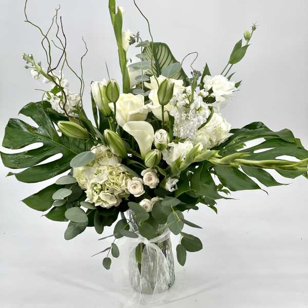 White floral arrangement in a clear glass vase with large green leaves