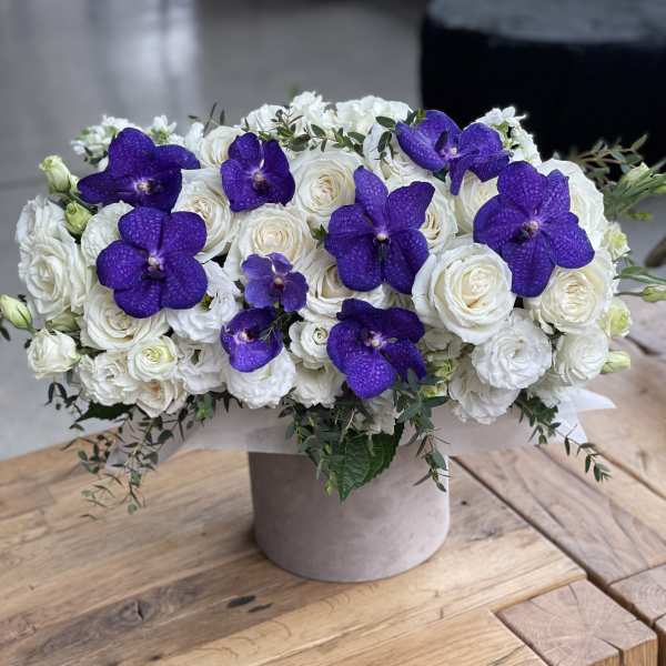 White roses and purple orchids arranged in a round vase