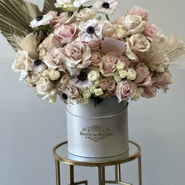 Blush and cream roses arranged in a round hatbox with dried accents