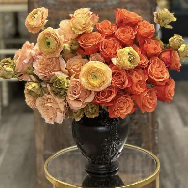 Bouquet of orange and peach roses with yellow ranunculus in a black vase