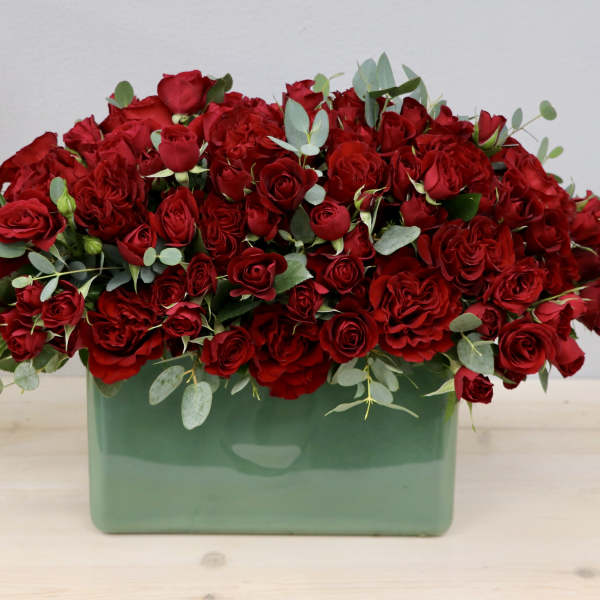 Dense red rose arrangement in a green rectangular vase