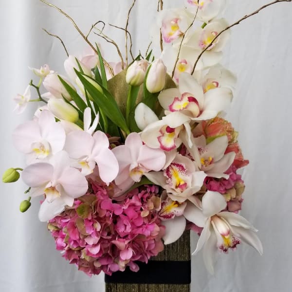 Tall floral arrangement with orchids and pink hydrangeas in a gold vase