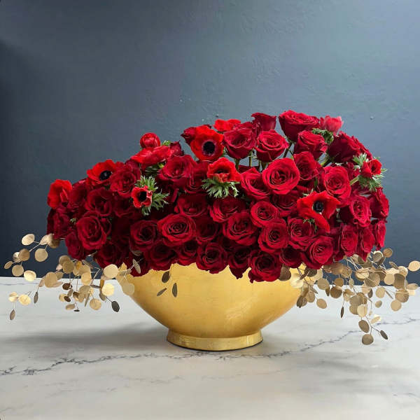 Red rose arrangement in a gold bowl with trailing dried foliage