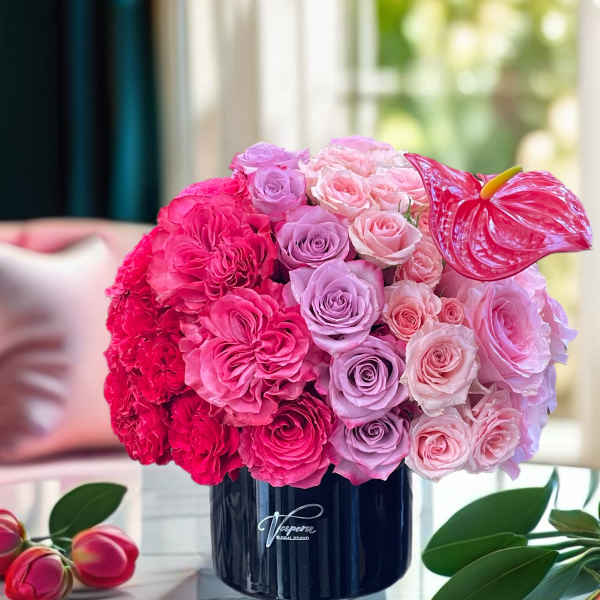 Pink and lavender rose arrangement in a dark vase with an anthurium bloom