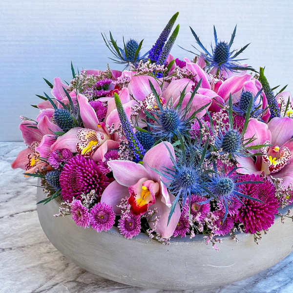 Pink orchid and purple flower arrangement in a low white bowl