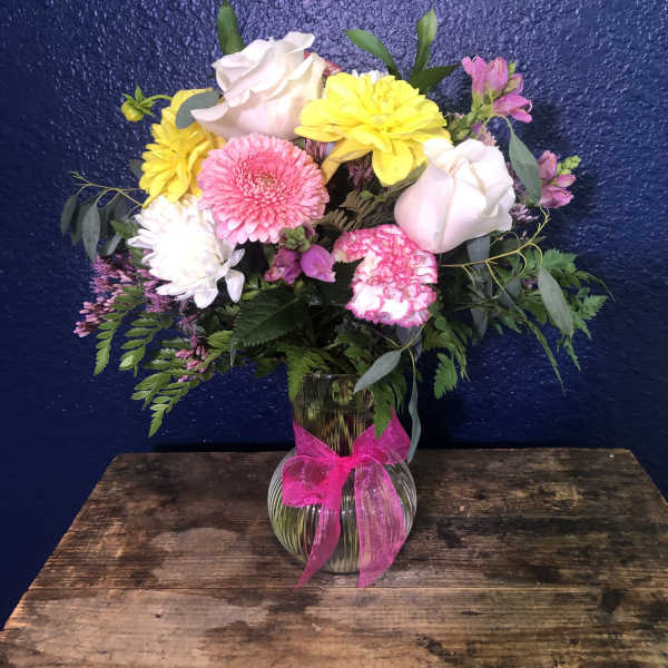 Mixed pink, yellow, and white flowers in a glass vase with a pink ribbon.