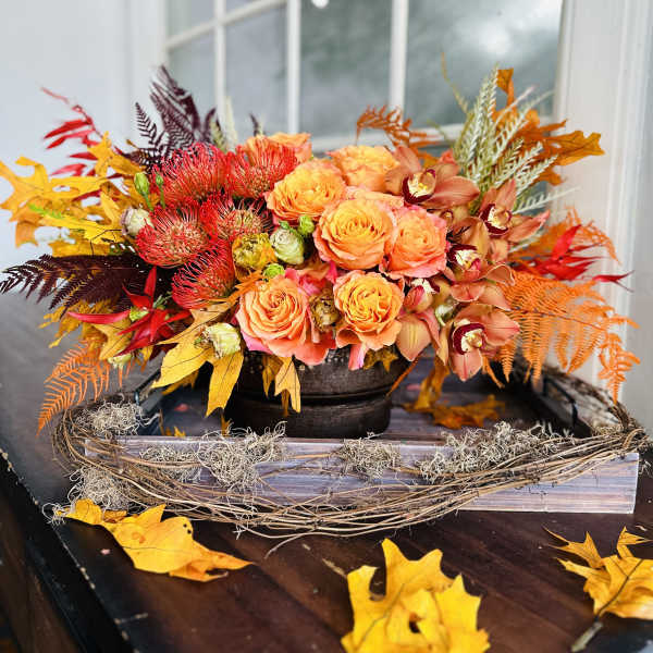 Autumn floral arrangement with orange roses and orchids in a low container