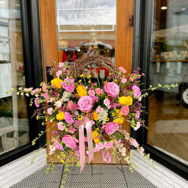 Large pink and yellow floral wreath on a stand with a ribbon
