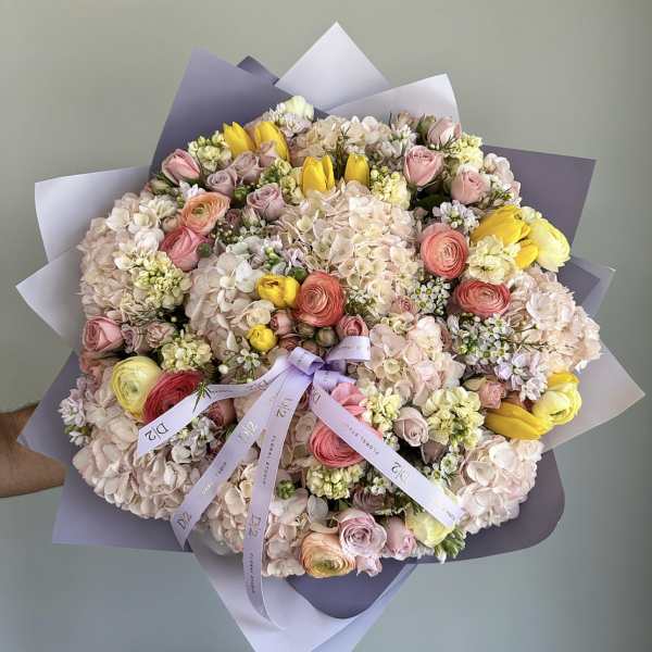 Large pastel bouquet of roses, hydrangeas, and yellow tulips wrapped in lavender paper