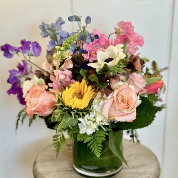 Mixed bouquet in a green glass vase with pink, purple, blue, and yellow flowers