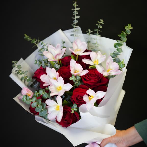 Bouquet of red roses and pale pink tulips wrapped in white paper