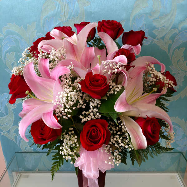 Red roses and pink lilies arranged in a tall vase with baby's breath