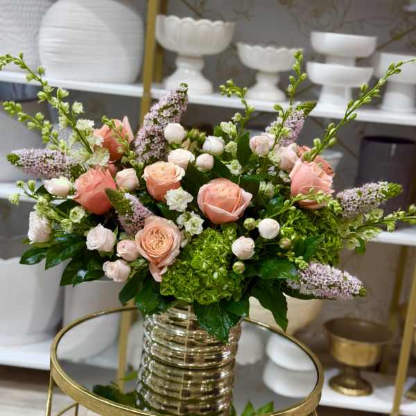 Peach and blush roses in a clear ribbed vase with green hydrangea and lilac spikes