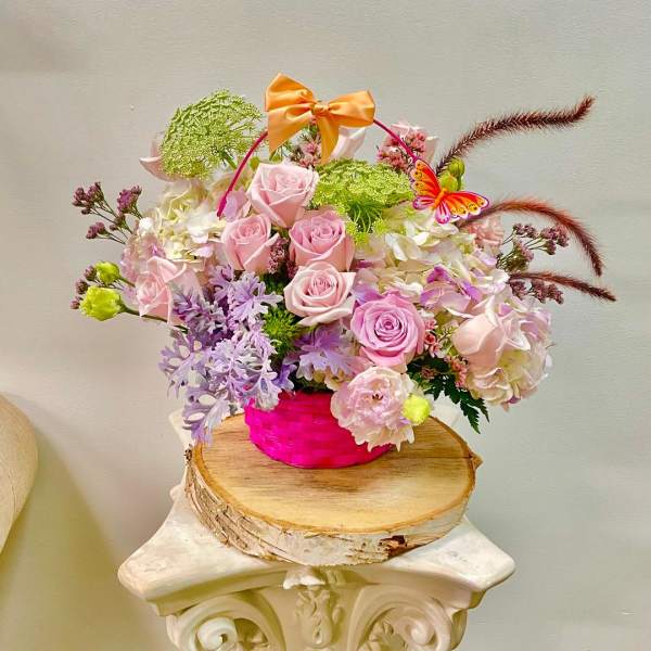 Pink roses and pastel flowers in a bright pink basket with a bow