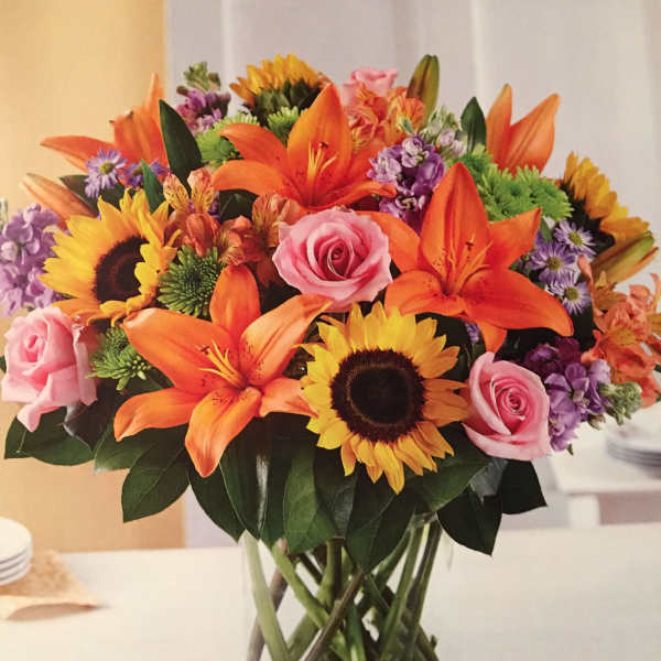 Mixed bouquet of sunflowers, orange lilies, and pink roses in a glass vase