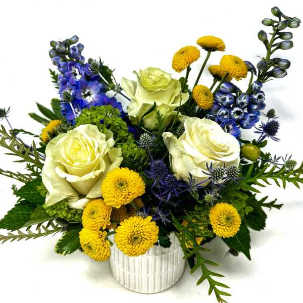 White roses, yellow pom flowers, and blue blooms in a white vase