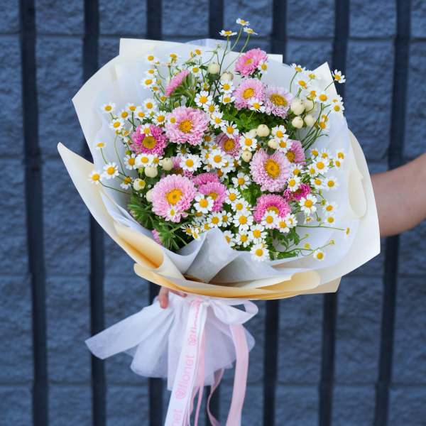 Pink daisy bouquet wrapped in white paper with a pink ribbon