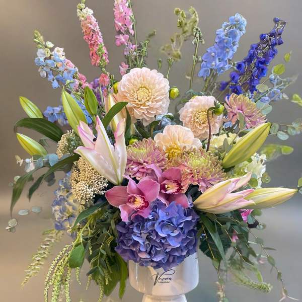 Mixed bouquet of pastel and blue flowers in a white pedestal vase