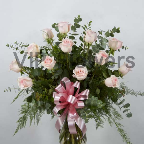Pink roses arranged in a glass vase with a pink ribbon bow