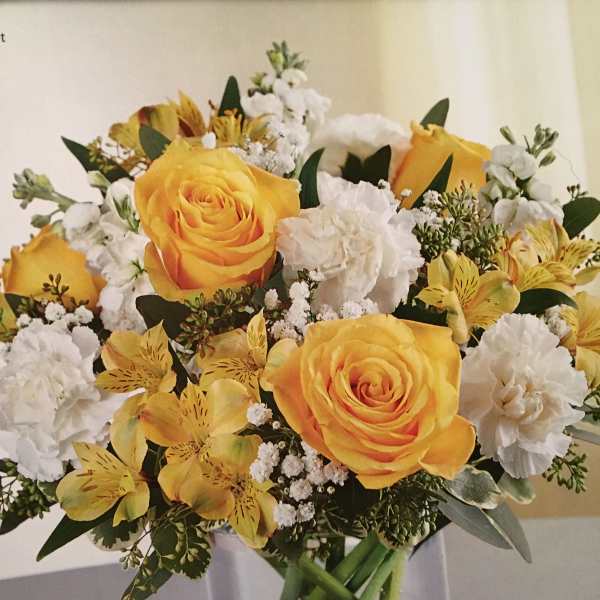 Yellow roses and white flowers arranged in a clear glass vase