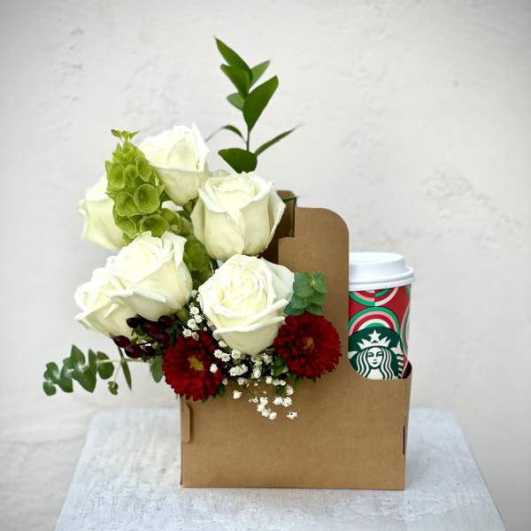 White roses with red flowers in a brown gift box beside a Starbucks cup