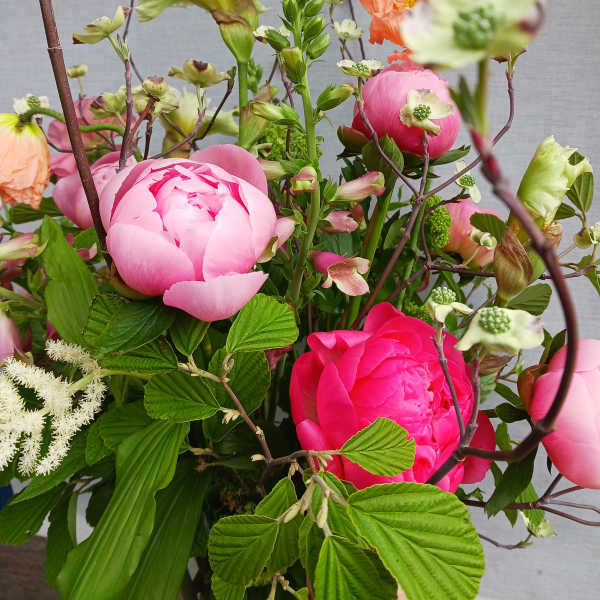 Loose arrangement of bright pink peonies with peach poppies and mixed blooms