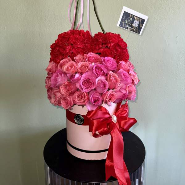 Heart-shaped floral arrangement of red carnations and pink roses in a pink box