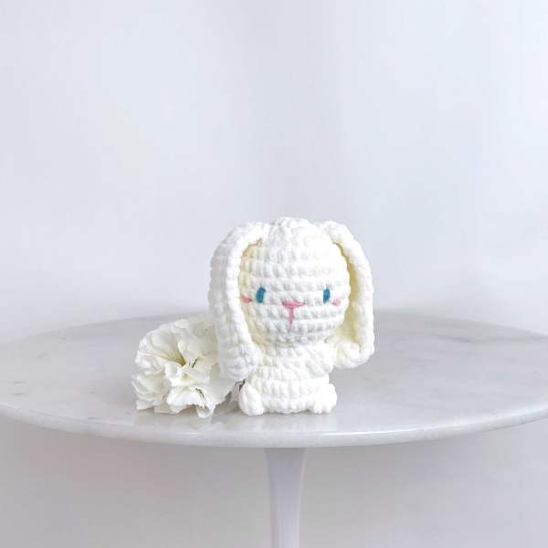 White plush bunny figurine beside a white carnation on a round table
