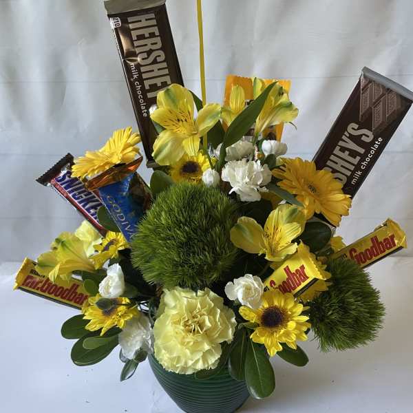 Yellow flowers and chocolate bars arranged in a green pot.