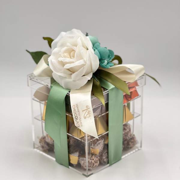 Gift box topped with white and teal flowers and satin ribbons