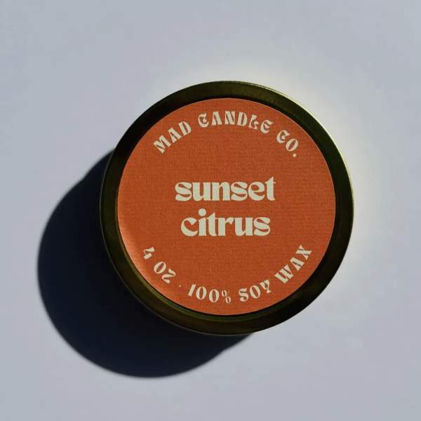 Round candle tin labeled "sunset citrus" on a plain surface