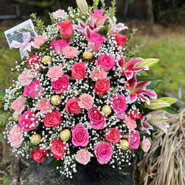 Pink roses and lilies arranged with baby's breath and gold chocolates