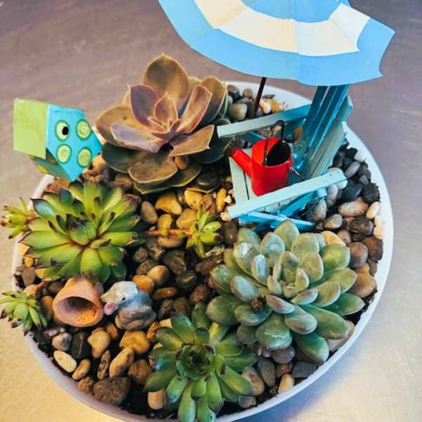 Succulent arrangement in a white bowl with a tiny beach chair and umbrella