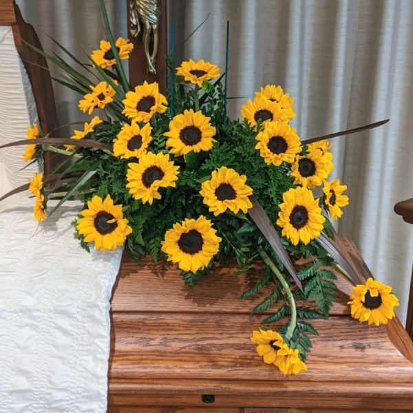 Sunflower arrangement displayed beside a wooden cross on a casket