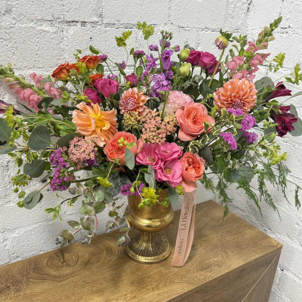 Large mixed bouquet in a gold vase with pink, orange, and purple flowers