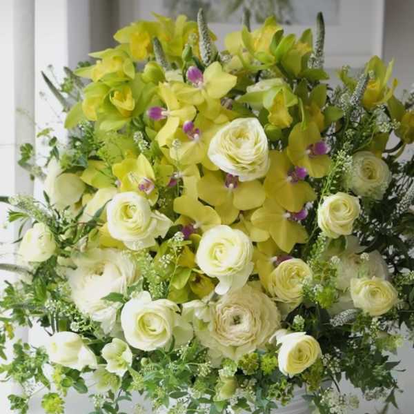 Yellow orchid and white ranunculus arrangement in a white bowl vase