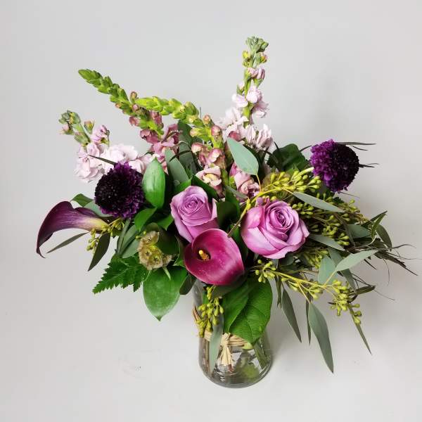 Pink roses and calla lilies in a glass vase with purple blooms