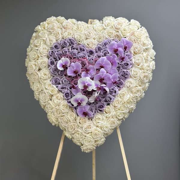 Heart-shaped floral arrangement of white and lavender roses with purple orchids