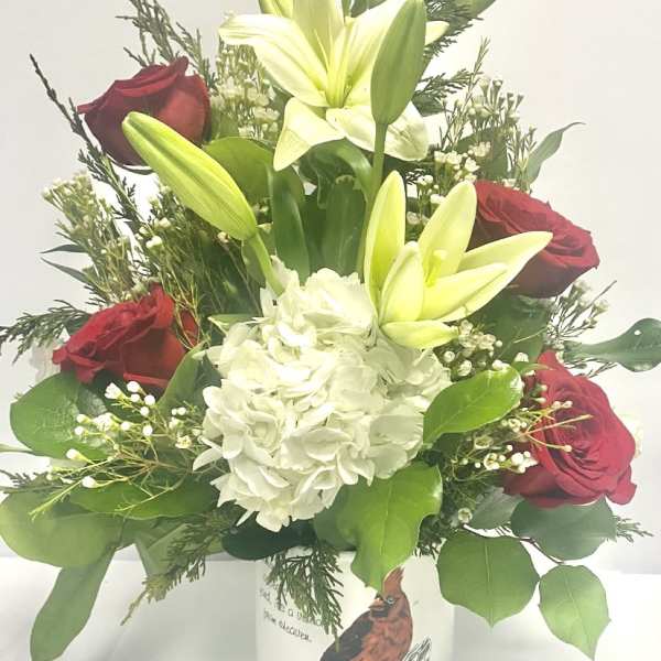 Red roses and white lilies in a white vase with a hydrangea bloom