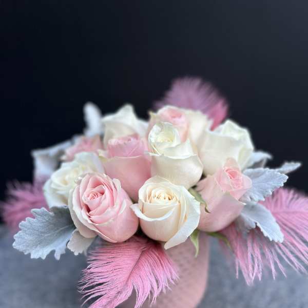 Pink and white roses arranged in a small round vase with feathers