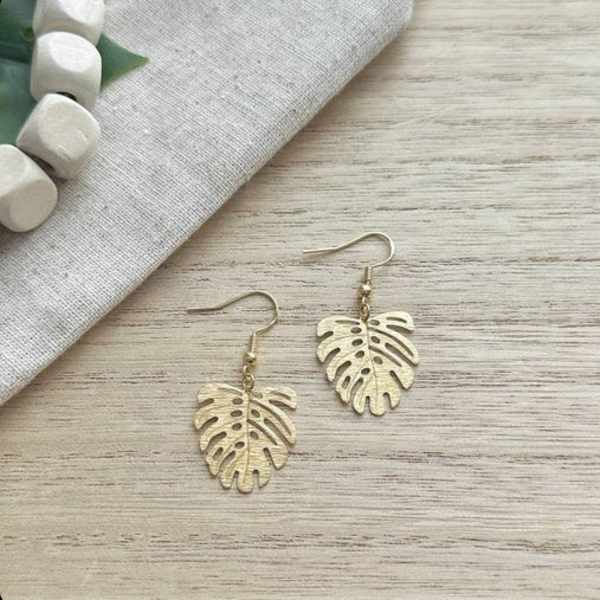 Pair of gold leaf-shaped dangle earrings on a wood surface